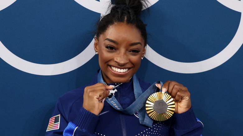 Simone Biles smiling with gold medal, goat charm