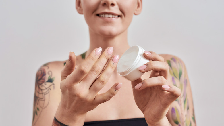 person with tattoos holds tub of lotion