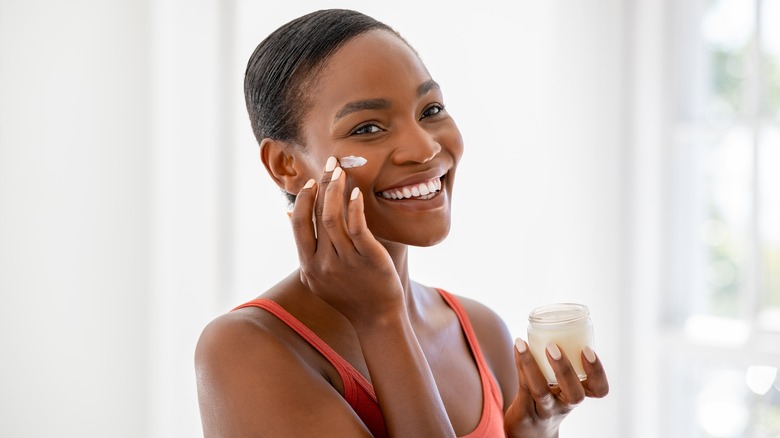 A woman applying skincare while smiling. 