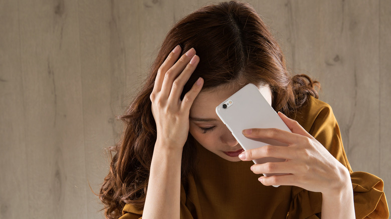 woman holding phone looking sad