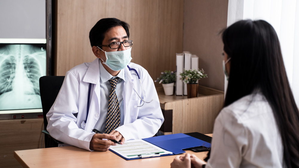 Male doctor in glasses and face mask consulting with female patient with long hair