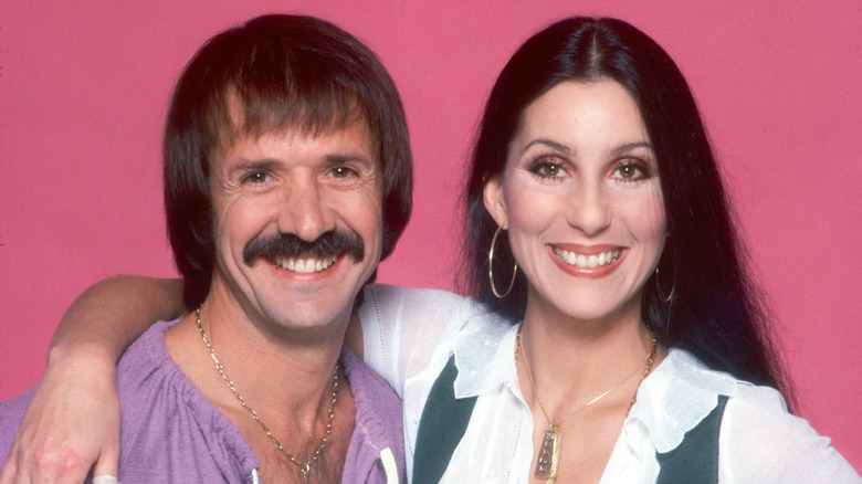 Sonny Bono and Cher smiling against a pink background