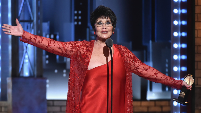 Chita Rivera with arms outstretched, speaking into microphone