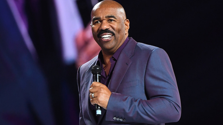 Steve Harvey in suit, smiling, holding microphone