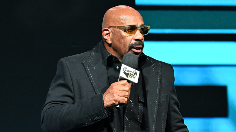 Steve Harvey holds mic onstage Invest Fest