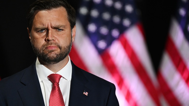 JD Vance scowling in front of American flags