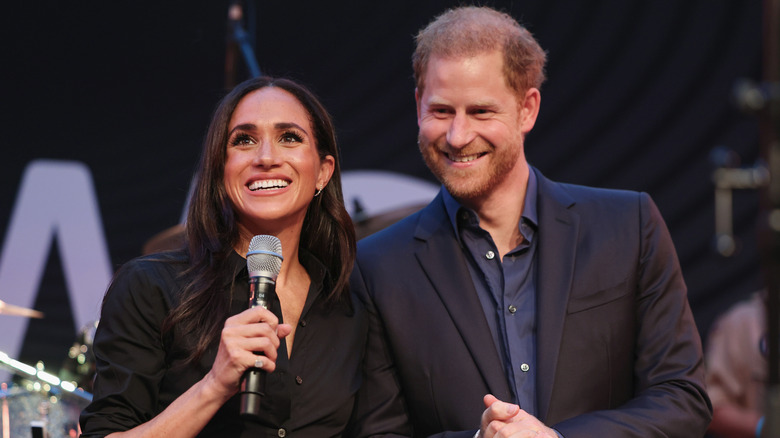 Meghan Markle and Prince Harry smiling and holding mic on stage during the 2023 Invictus Games in Germany