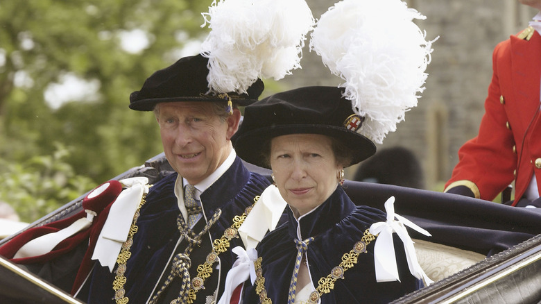 King Charles and Princess Anne in carriage wearing feather hats  