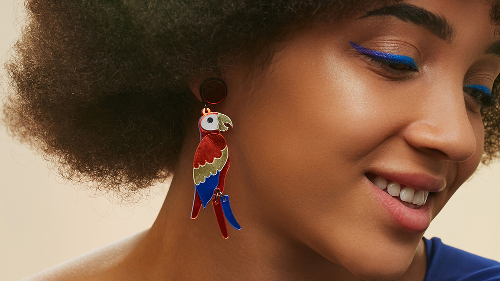 Closeup of a woman with navy liner and a peach toned eye shadow with a parrot earring