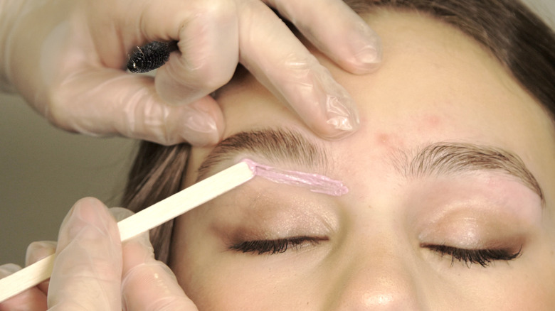 Esthetician applying wax under an eyebrow