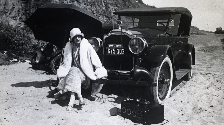 Woman sitting on car at beach 1924