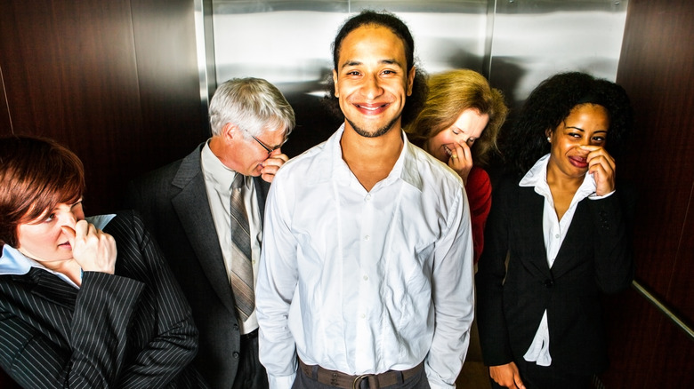 man smiling in elevator as others hold their noses