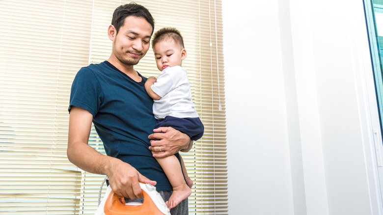 single father holding child and ironing