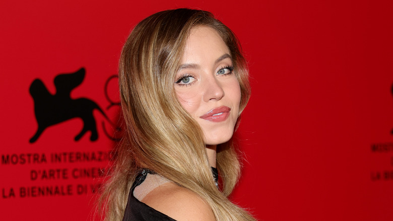 Sydney Sweeney smiling over her shoulder on a red carpet