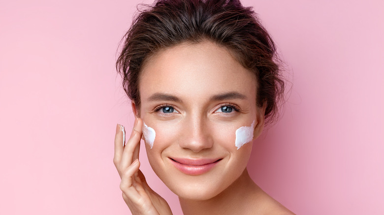 woman apply cream to face pink background