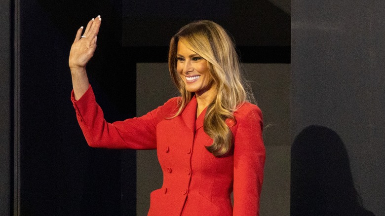 Melania Trump smiling and waving in a red suit