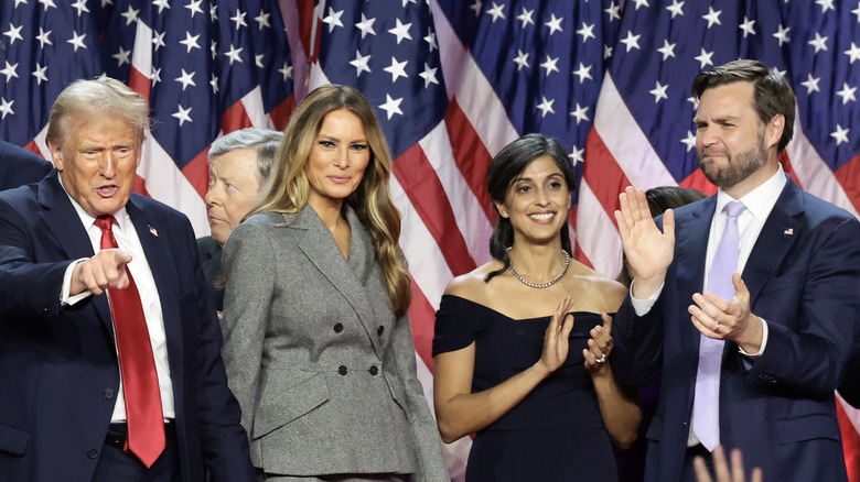 Melanie Trump standing in front of a row of American flags with Donald Trump, JD Vance, and Usha Vance