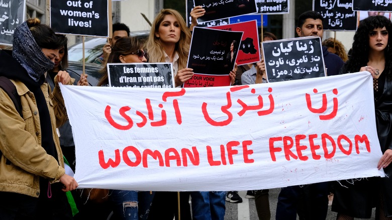 women holding protest signs that read "woman life freedom" in multiple languages