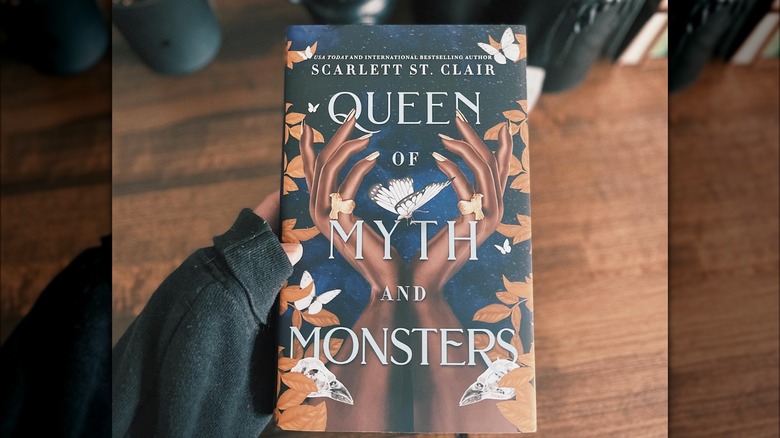 Image of a hand holding a copy Queen of Myth and Monsters