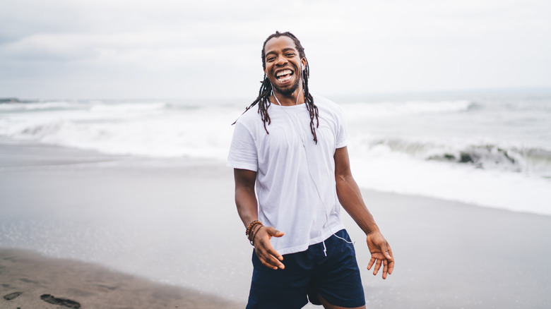 Black man laughing on beach, listening to earphones