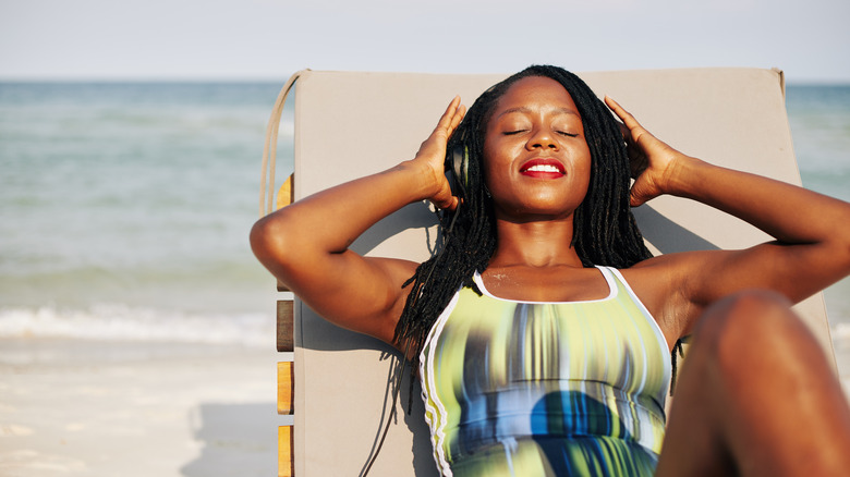 Black woman relaxing on lounge chair on beach with headphones