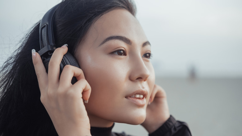 Close up of Asian woman with black headphones, beach in background