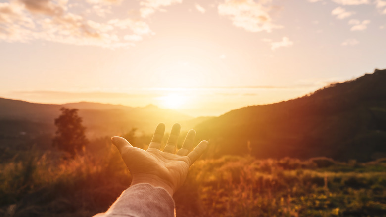 Hand reaching out to sunrise