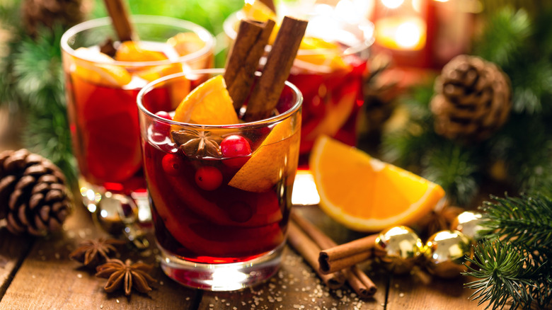 glasses of mulled christmas wine sit on wood table surrounded by pine