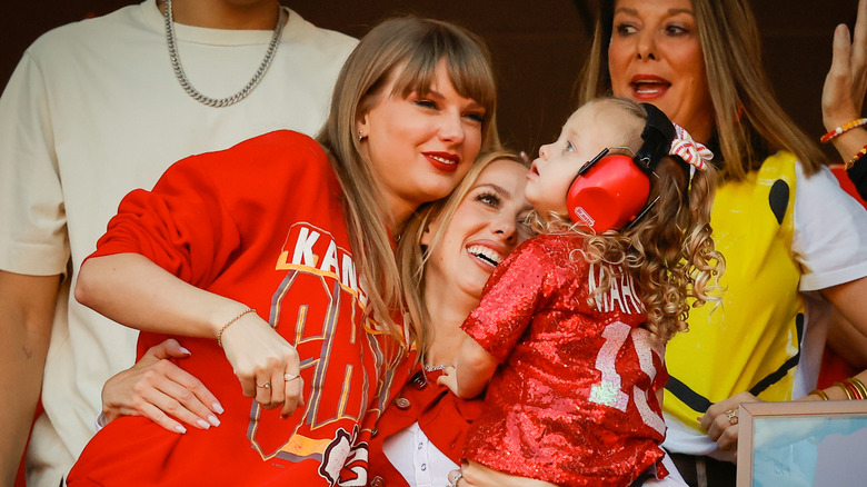 Taylor Swift and Brittany Mahomes smiling and hugging while holding Mahomes' daughter