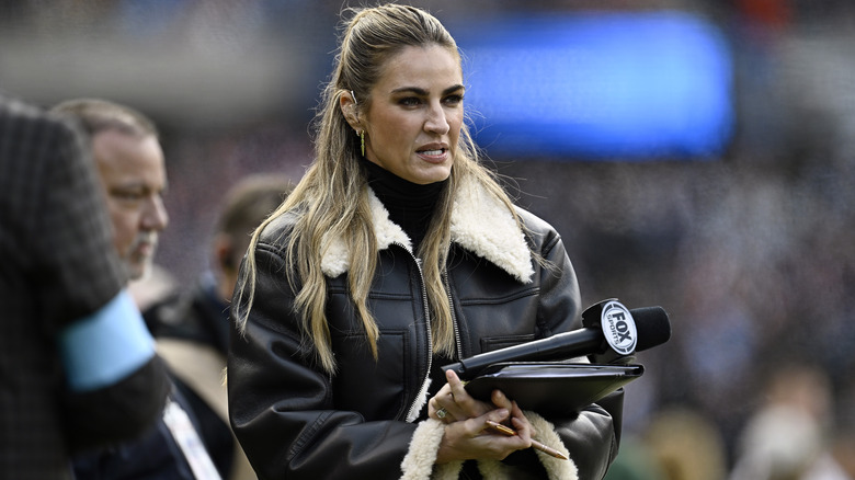 Erin Andrews wearing coat holding microphone and binder