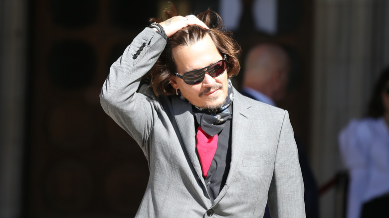 Johnny Depp runs his fingers through his hair wearing a grey suit and sunglasses