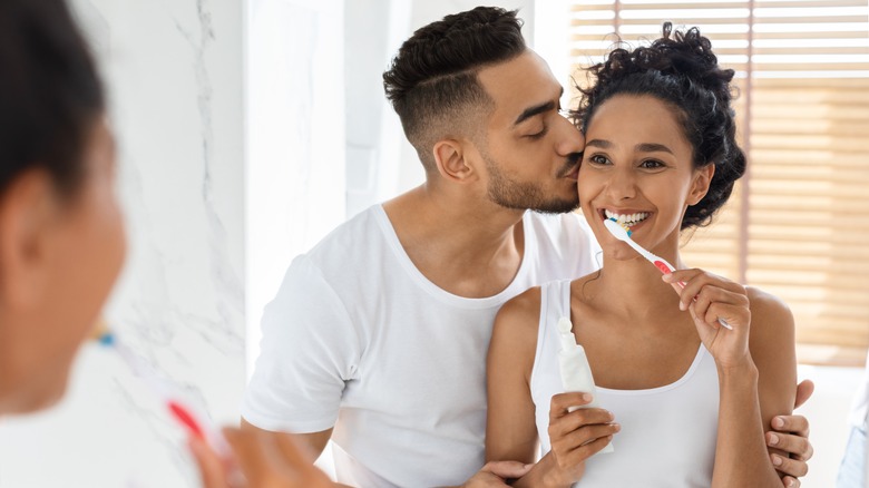 man kissing girlfriends cheek, brushing teeth