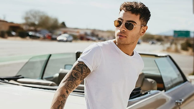 Man with dark hair, wearing sunglasses and leaning against convertible