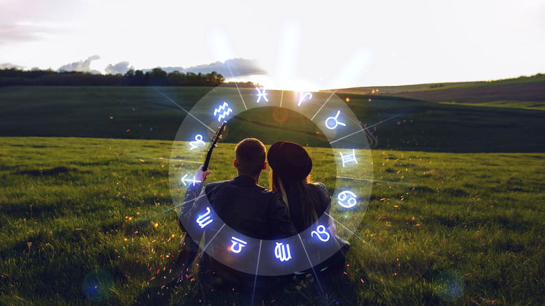 Two people sitting close together in a field with the zodiac wheel around them 