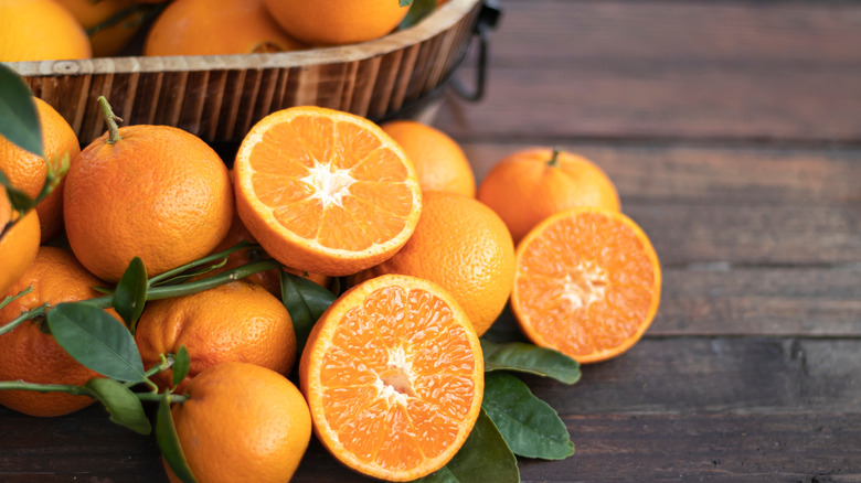 Oranges on table next to basket of more oranges