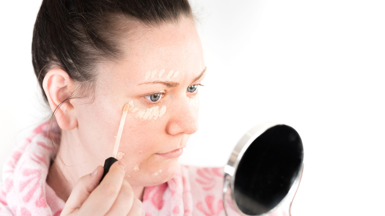 Woman applying concealer to undereyes