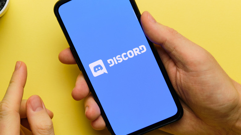 Person holds phone showing Discord logo