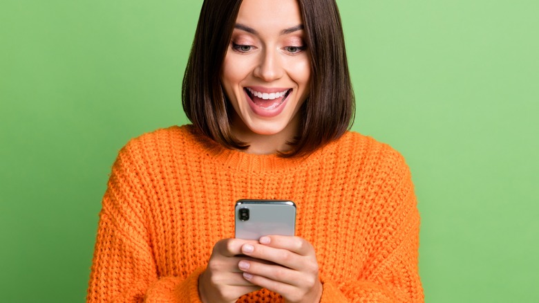 Woman in orange sweater smiles at phone