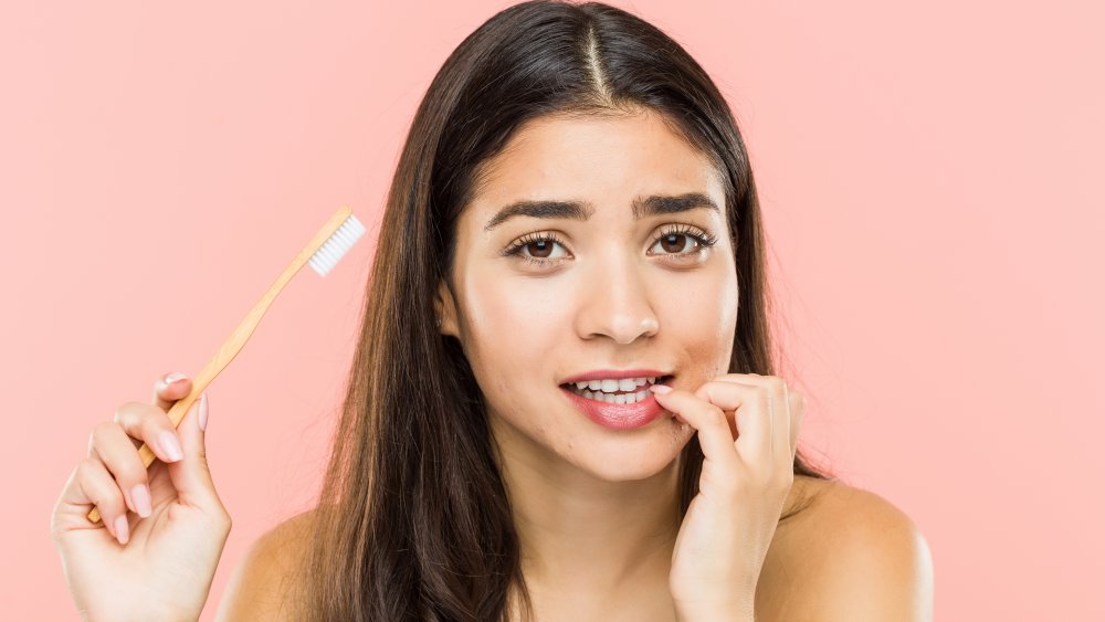 a woman biting her fingernails and holding a toothbrush