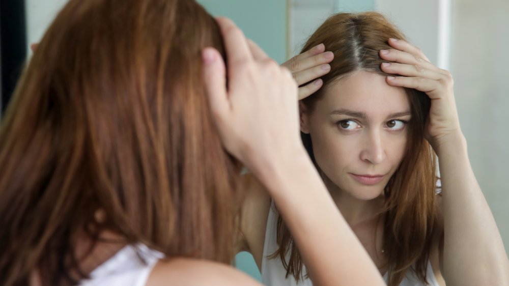 a woman looking at her gray hair in the mirror