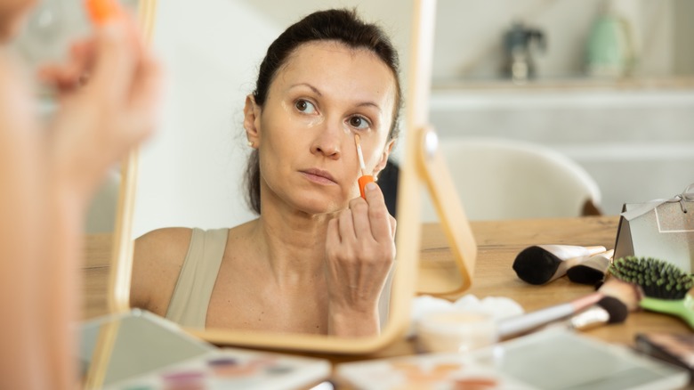 Woman applying concealer under eyes in the mirror