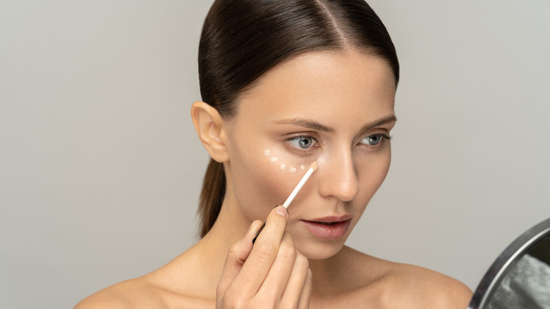 A woman using liquid concealer on her face