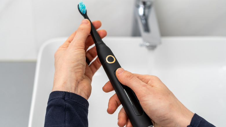 person holding electric toothbrush over sink