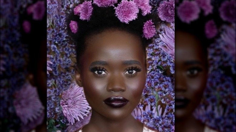 Black model wearing purple flowers and wearing Dehiya Beauty