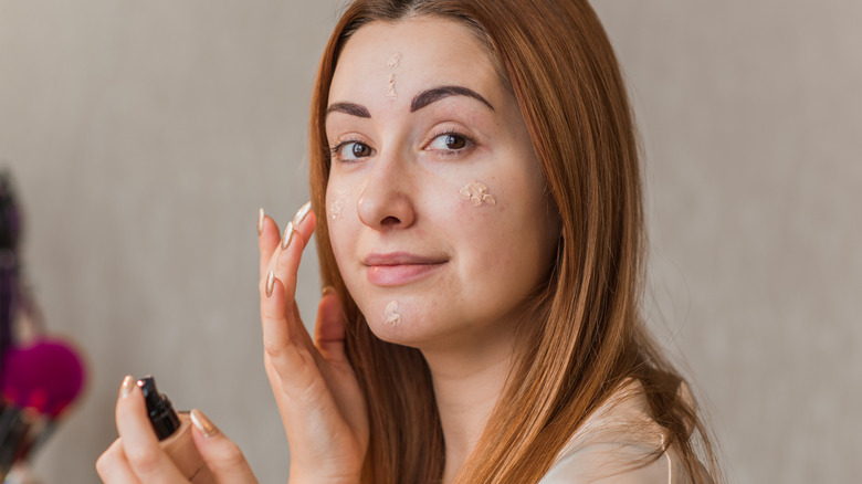 Woman with acne applying makeup