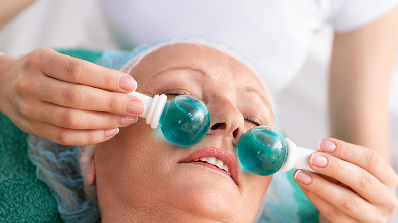 Woman using facial ice globe rollers during facial