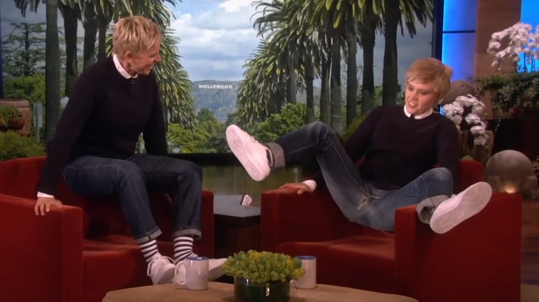 Kate McKinnon with short blonde hair, sitting contorted on Ellen's chair