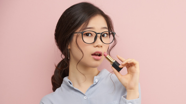 Woman putting on a pale pink lipstick