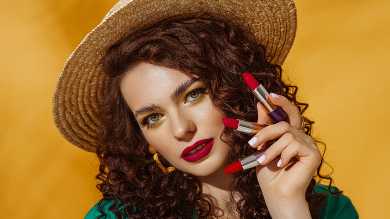 A woman holds up three red lipsticks