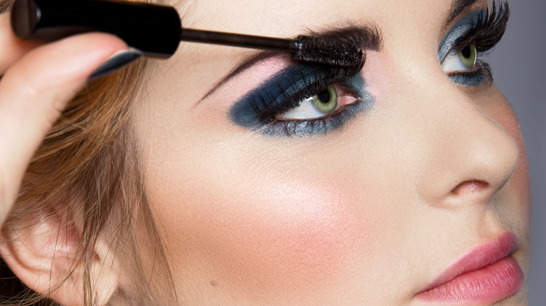 Woman wearing navy blue eyeshadow and getting mascara applied